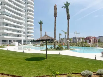 a resort with a pool and palm trees and a building at Moderno apartamento con vistas a la costa mediterranea en Gran Canet in Canet de Berenguer