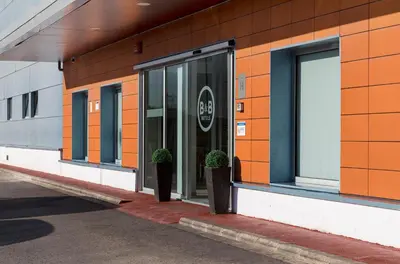 an orange building with two potted plants in front of it at B&B HOTEL Valencia Aeropuerto in Paterna