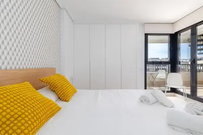 a white bedroom with a large bed with yellow pillows at ApartUP Patacona Sunrise Duplex I in Valencia