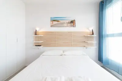 a white bedroom with a bed and a window at Global Vacacional, Apartamento con terraza y vistas a la costa mediterránea in Canet de Berenguer