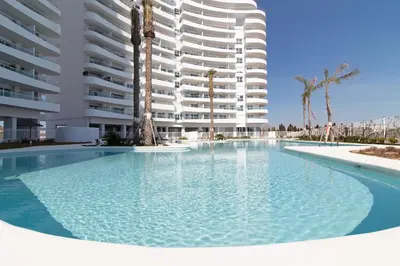 a swimming pool in front of a large apartment building at Global Vacacional, Apartamento con terraza y vistas a la costa mediterránea in Canet de Berenguer