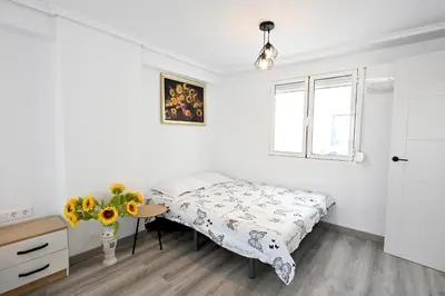a white bedroom with a bed and a table and a window at Victoria Apartment in Puerto de Sagunto