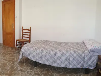 a bedroom with a bed and a chair and a door at Vacansis Habitaciones Privada en una Villa a un paso del Mar en Cullera in Cullera