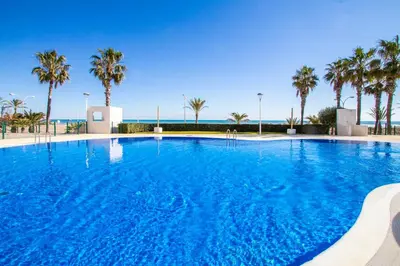 a large blue swimming pool with palm trees and the ocean at ESPACIO 15 - Primera Línea de Playa in Cullera
