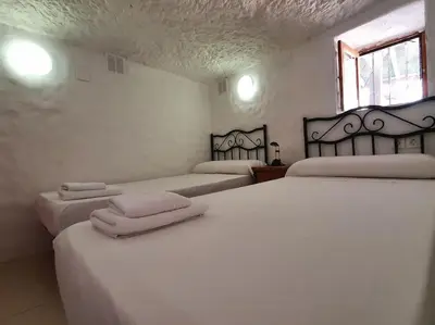 a room with three beds with white sheets and a window at LA CUEVA de TONI EL SECO in Paterna